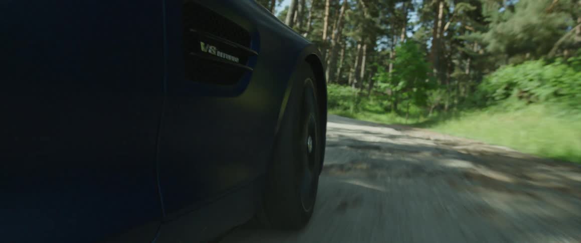 Sports car driving over a rural road through the forest at morning