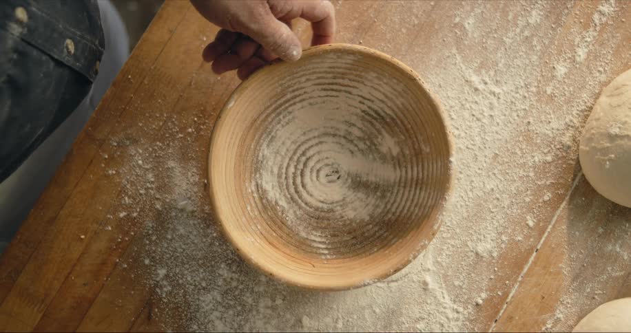 Man dusting a ceramic bowl with flour over a wooden table