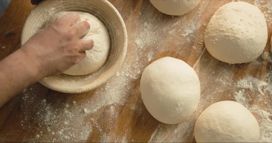 Chef knewding bread dough on a bowl over a wooden table