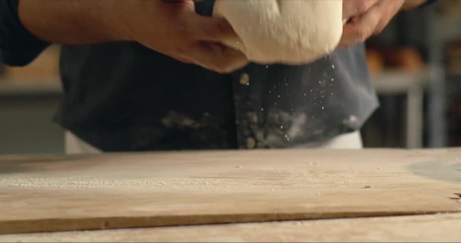 Man lifts up bread dough from a board over a table