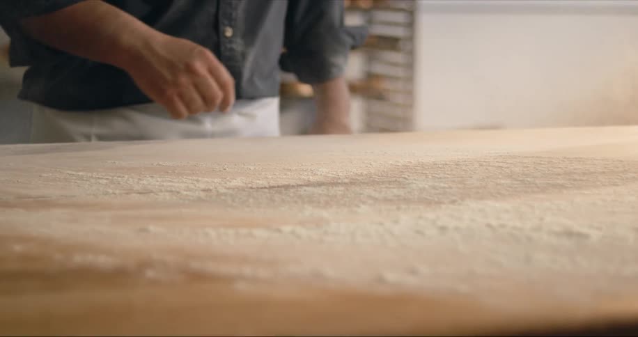 A baker custs a countertop with flour