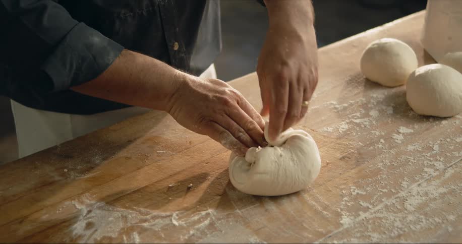 A man rolls and kneads a ball of dough on a floured table