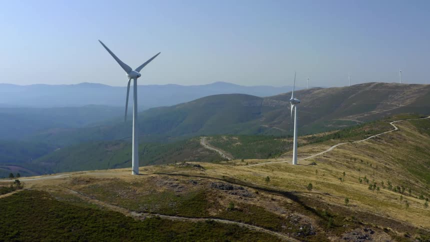 Wind turbines spin on top of tall hills in the countryside