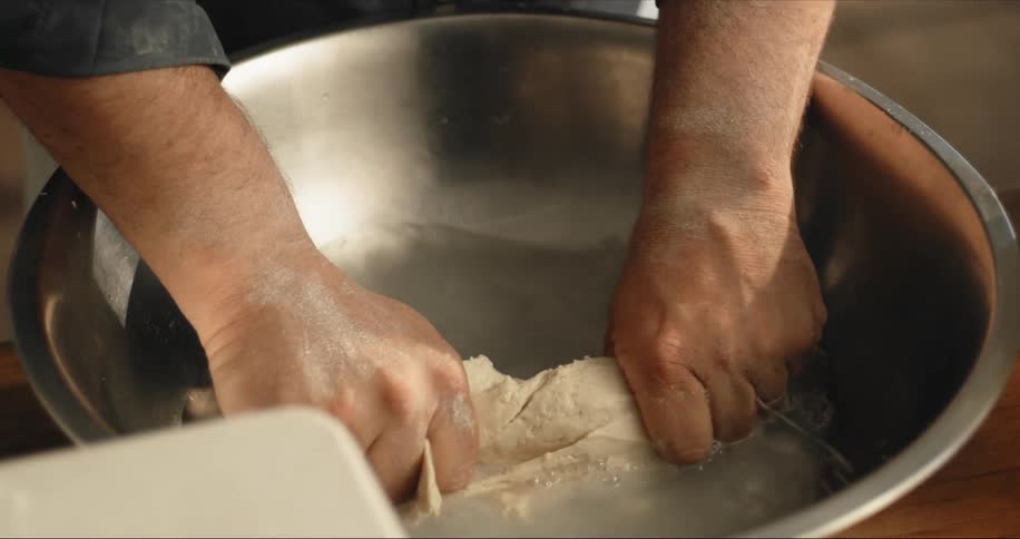A person kneading dough in a bowl of water on a table