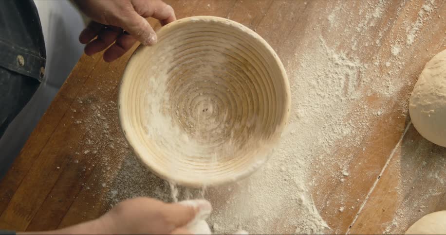 A baker dusts a bowl with flour