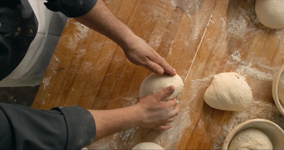 A man rolls dough to form loaves of bread