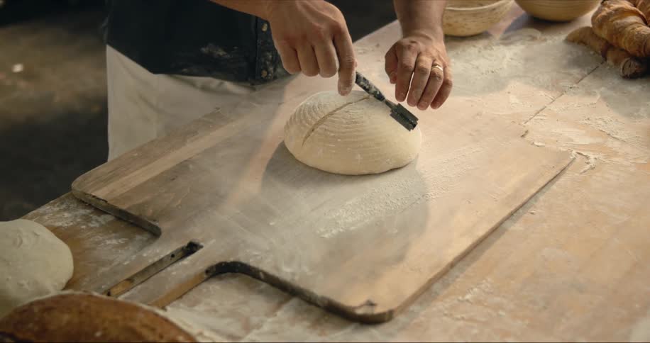 A baker is scoring bread dough with a knife