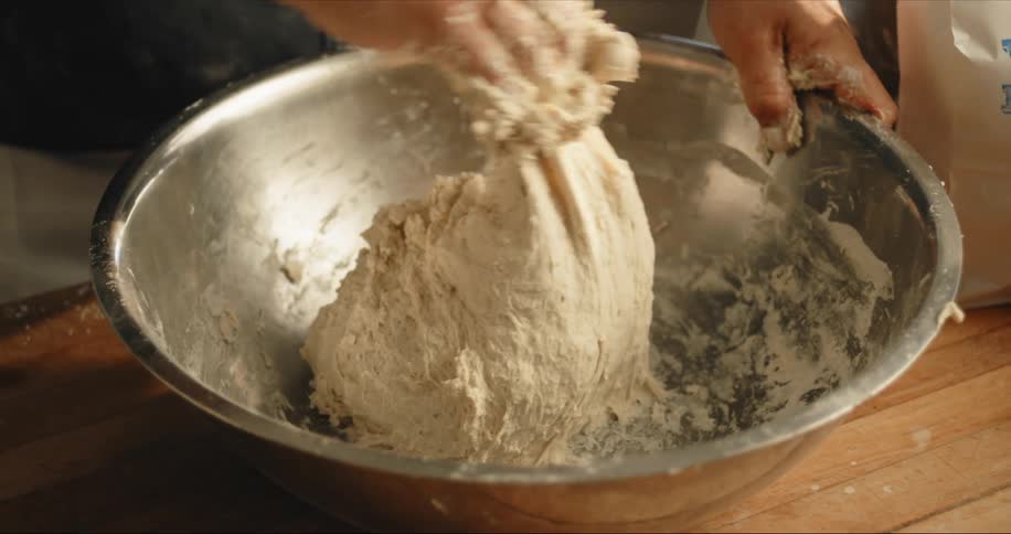 Chef kneading bread dough on a metallic bowl over a wooden table