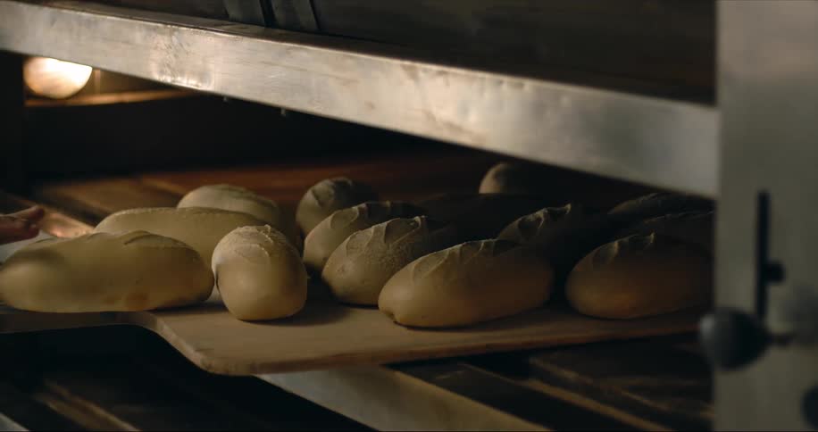 A man pulls loaves of bread out of a large commercial oven