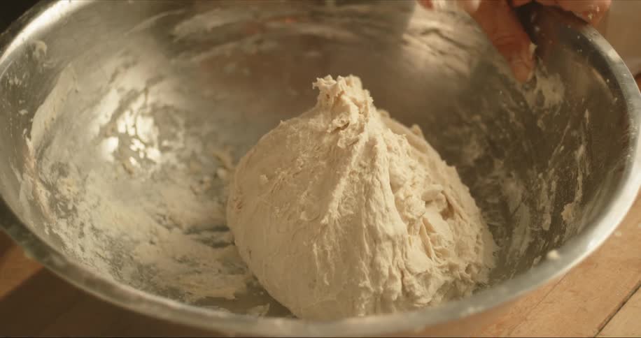 A person in a room kneading dough in a bowl on a table