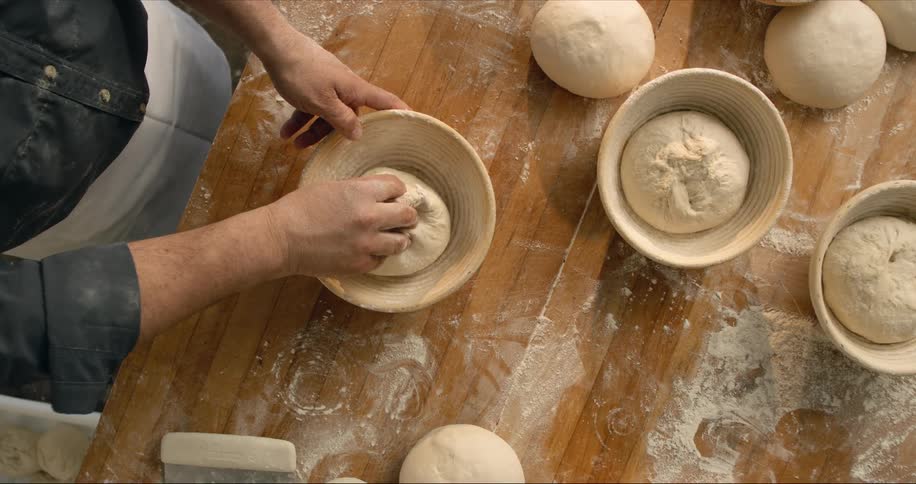 A baker is placing dough into bowls on a table