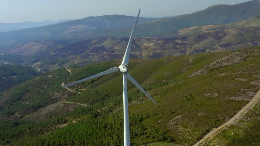 Wind turbines spinning on a wind farm with mountains in the distance