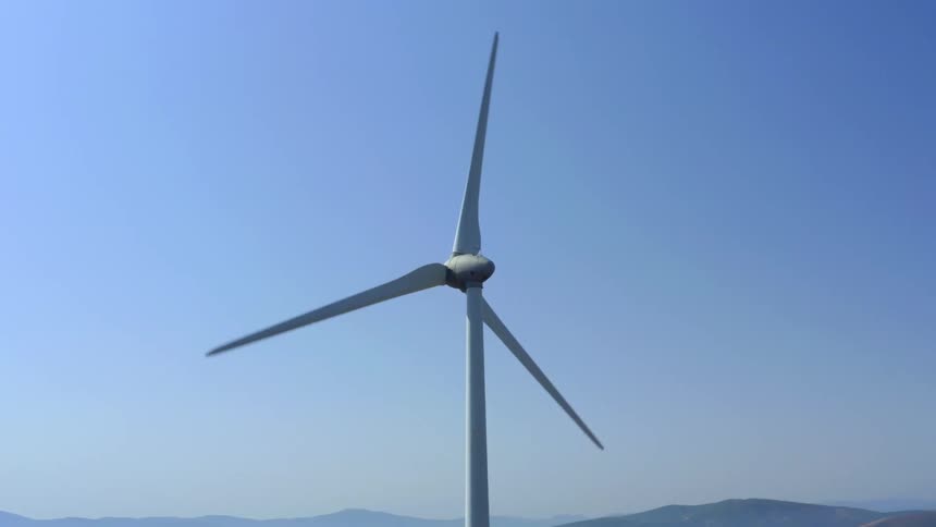 Wind turbine slowly turns with misty covered mountains and hills in background