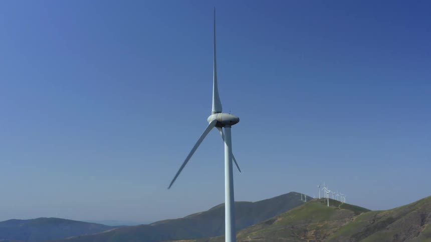 A wind turbine turning in the wind with hills the sky and clouds in the background