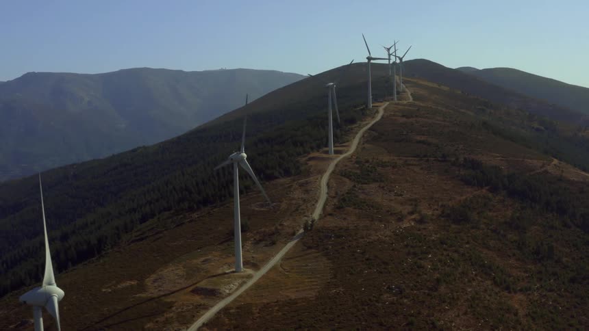 Aerial veiw of wind turbines spinning over a hill at evening