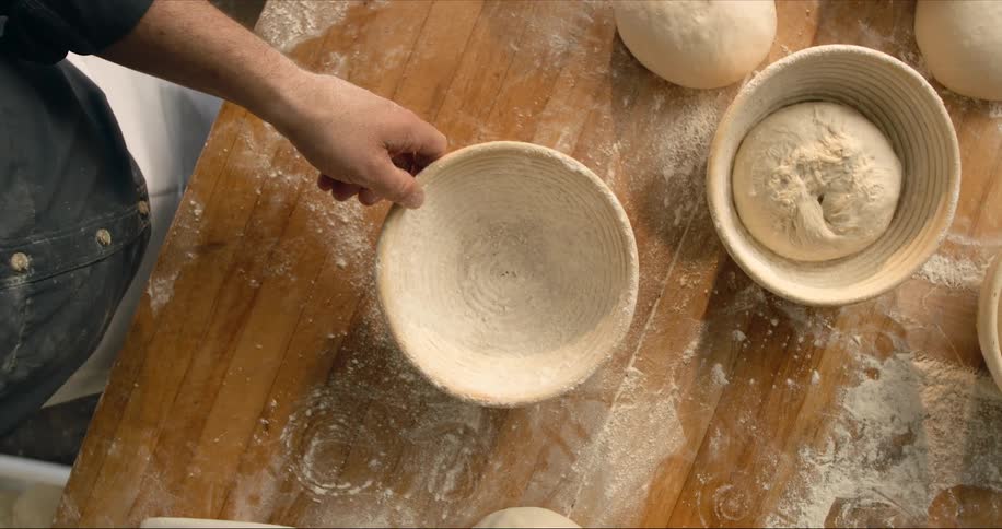 Top down view of a man dusting a bowl with flour and placing bread dough inside