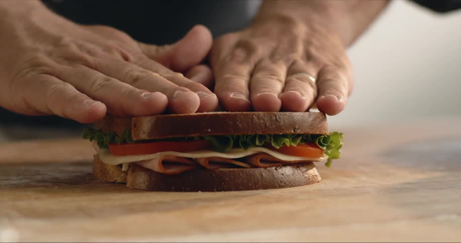 A man puts a piece of bread on top of a sandwich