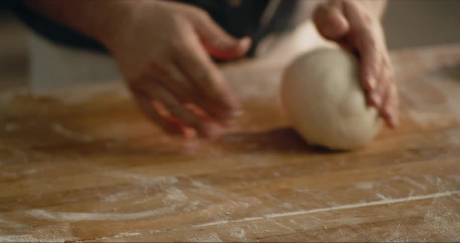 Man kneading bread dough over a wooden table