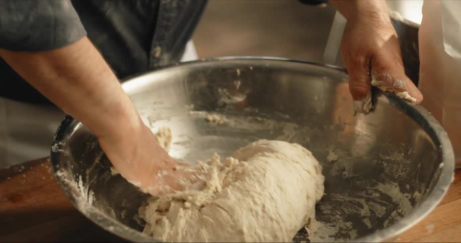 A man mixes a sticky dough with his hand in a large mixing bowl