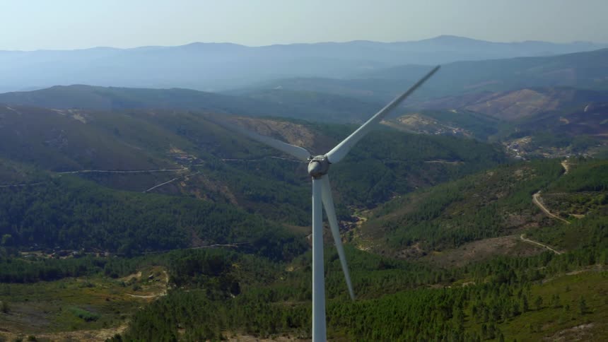 Fog covers mountains on horizon as wind turbine spins slowly above forest and valley