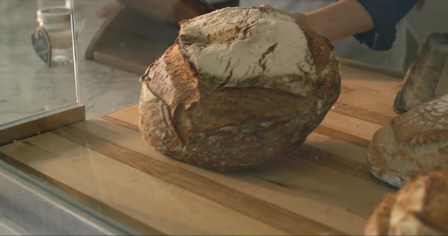 A baker places a large round loaf of bread on a wooden cutting board