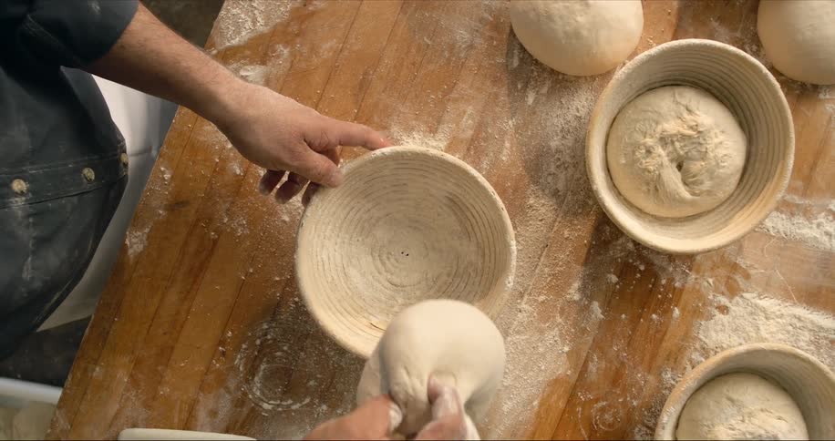 Chef placing a loaf of bread dough on a bowl over a wooden table