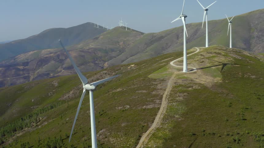 Wind turbines spinning on a wind farm with mountains in the distance