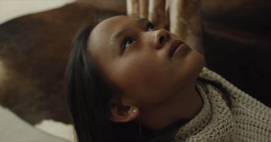 Close up of the face of a young woman wearing a gray sweater looking at the camera