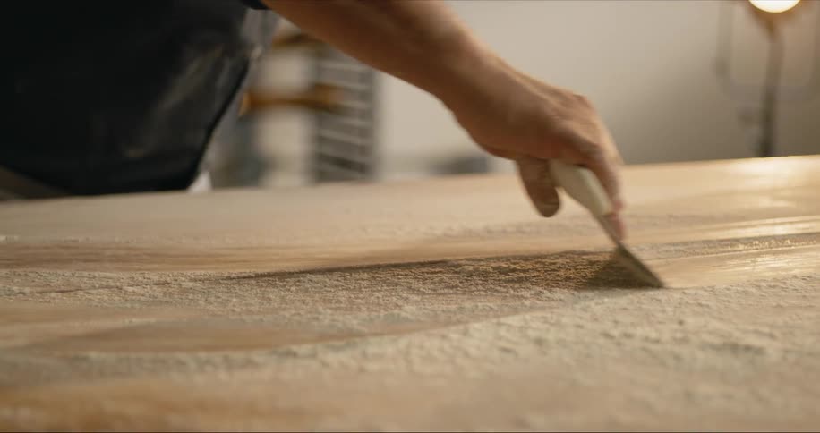 A baker uses a dough blade to remove flour off a counter