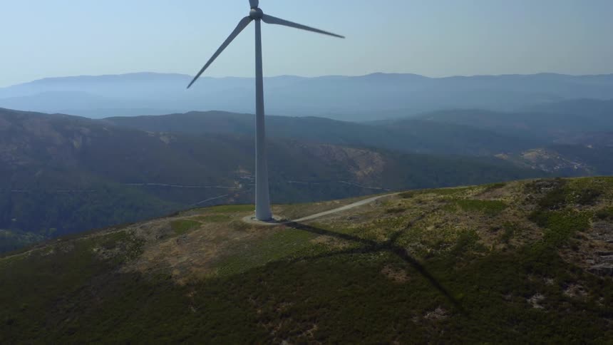 Aerial view of a wind turbine spinning on the top of a mountain at sunset