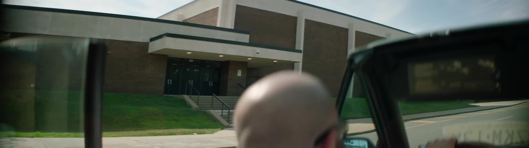 A man in a convertible drives past a school