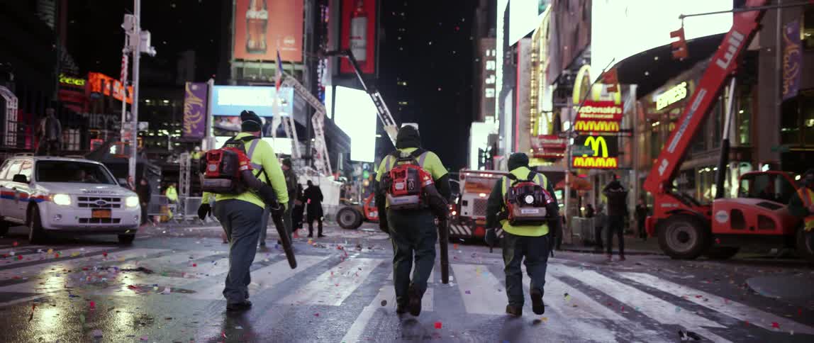 Workers use leaf blowers to clear confetti and debris from a street in times square