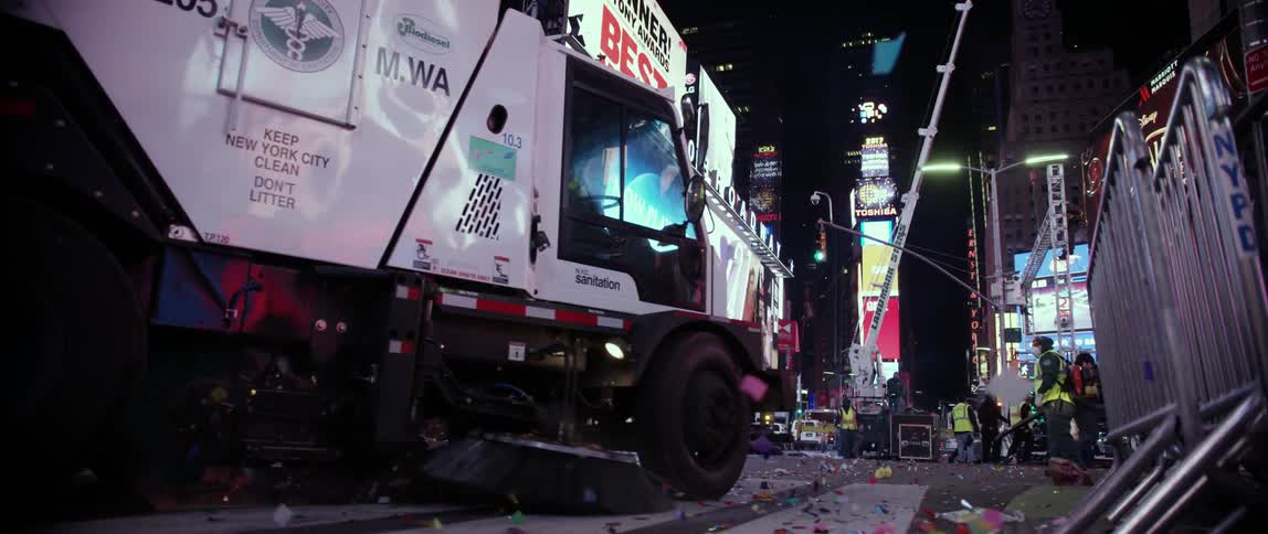 A sanitation vehicle and workers clean up parade debris