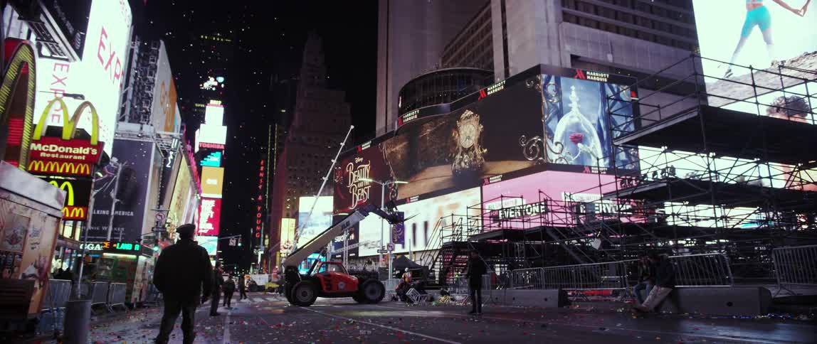 People walk along a busy city street with large screens on a building