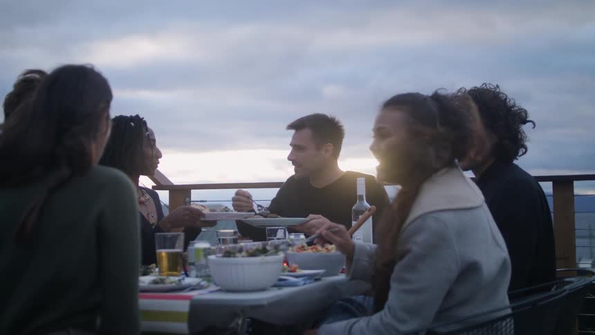 A group of young adults sit at a rooftop table eating food