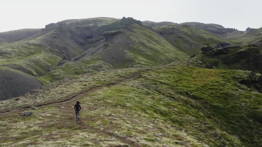 A jogger is running across a mountain ridge with mountains in the distance