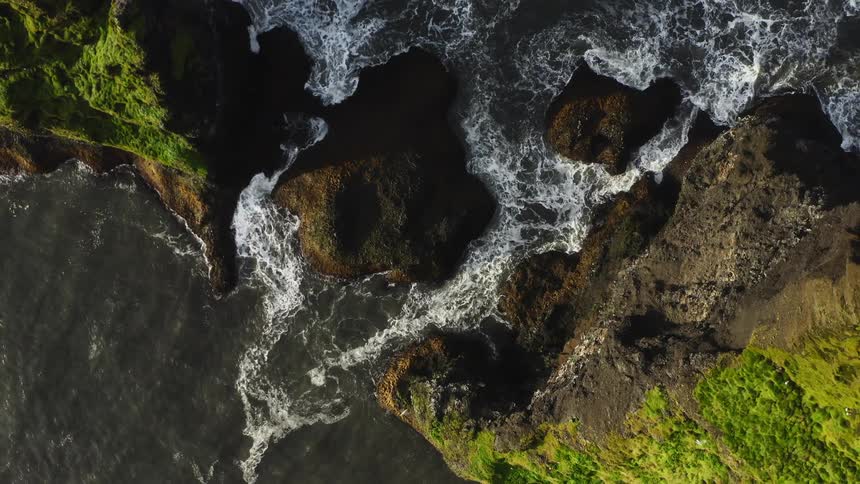 Aerial view of sea waves breaking against cliff rocks