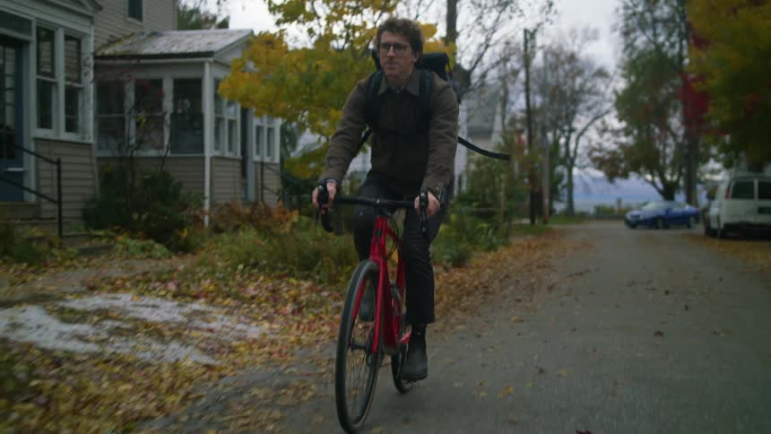 Man driving a red bicycle on a road in the neighborhood at fall