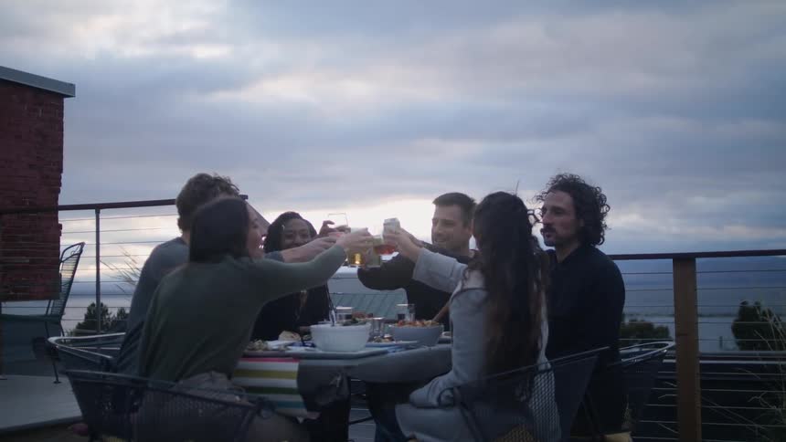 Group of happy friends drinking and toasting with drinks on a table in the purch at sunset