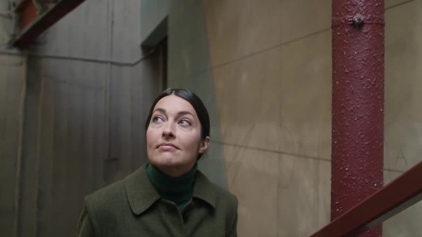 Woman wearing a green coat walking up the stairs of a building