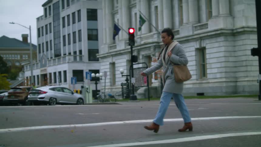 A woman walks across a city street as cars are stopped for her