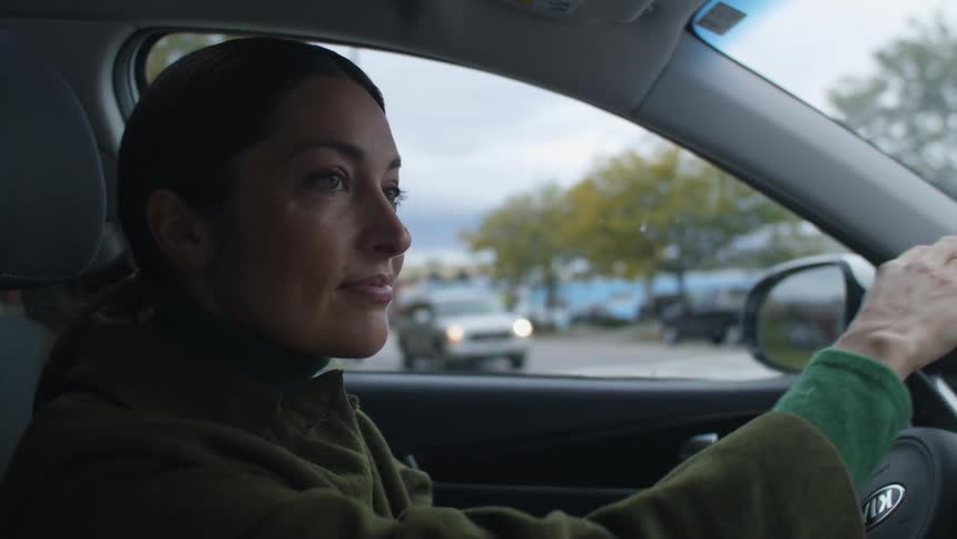 A woman smiles as she turns her car around a corner