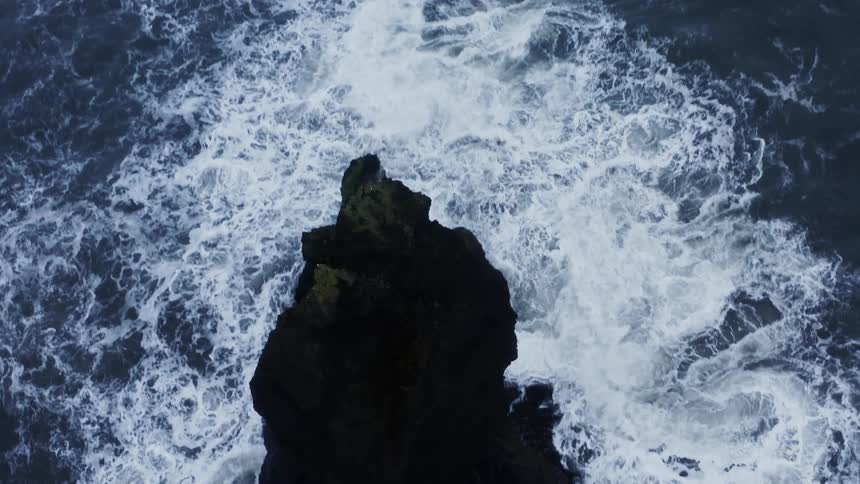 An aerial view of ocean water crashing against coastal rocks during the day