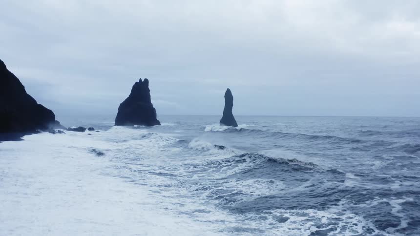 Waves rolling in to the coast past large rocks in the water