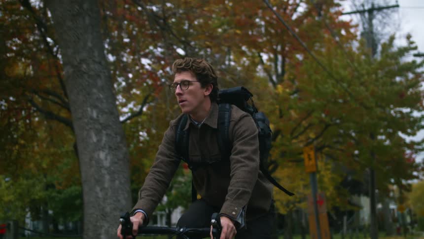 A man with a backpack on a bicycle with trees houses the sky and clouds in the background