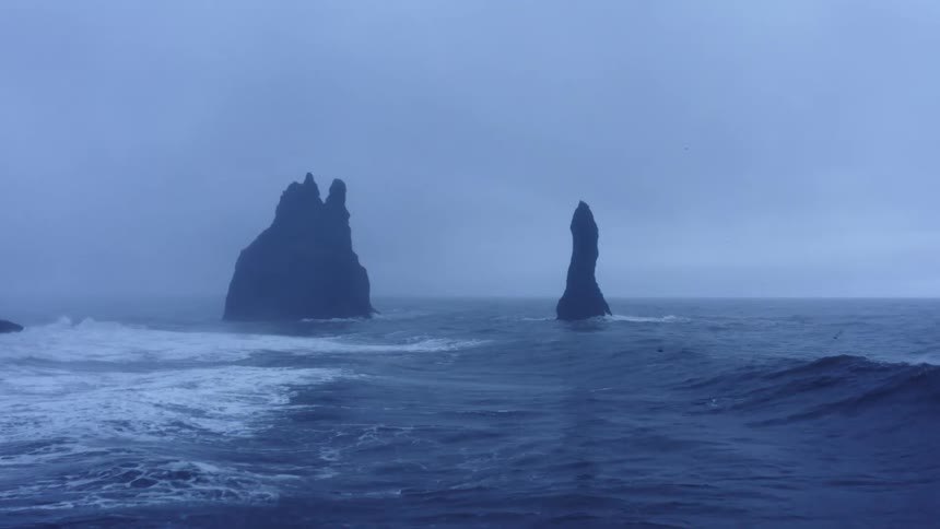 Aerial view of rock promontory over the ocean surrounded by fog near the coast