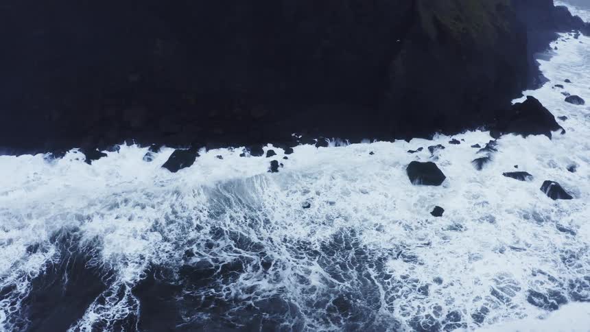 Strong sea waves wash onto the shore below a cliff