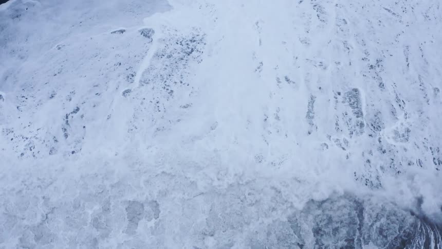Aerial view of foamy ocean waves breaking against the shore