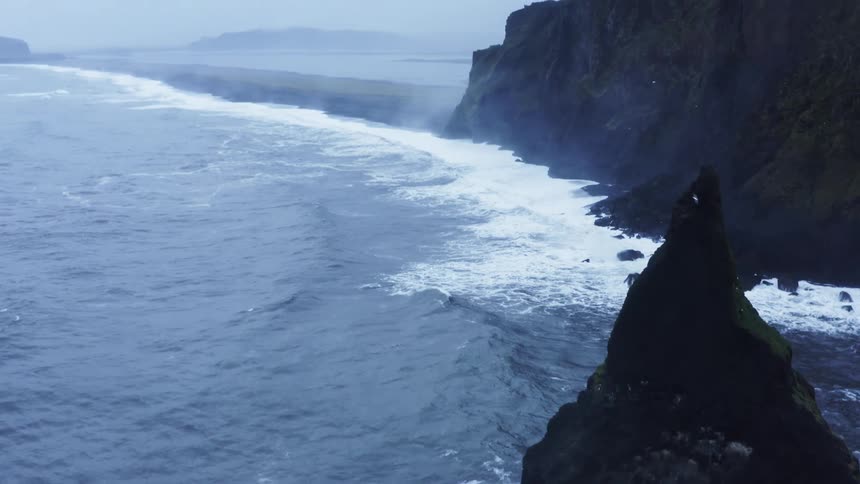 Waves splash against rock formations as they roll in shore under a cloudy sky