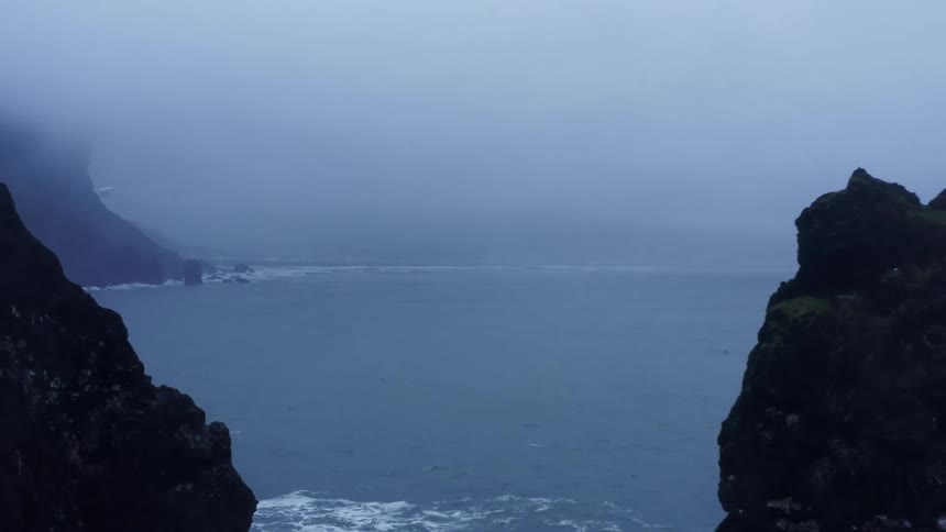 Aerial view of foggy wavy sea next to coast